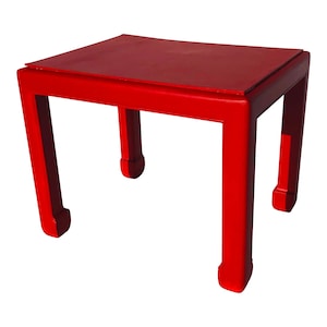 May include: A red lacquered side table with a square top and four legs. The legs are shaped like a stylized 'C' and have a rounded bottom.