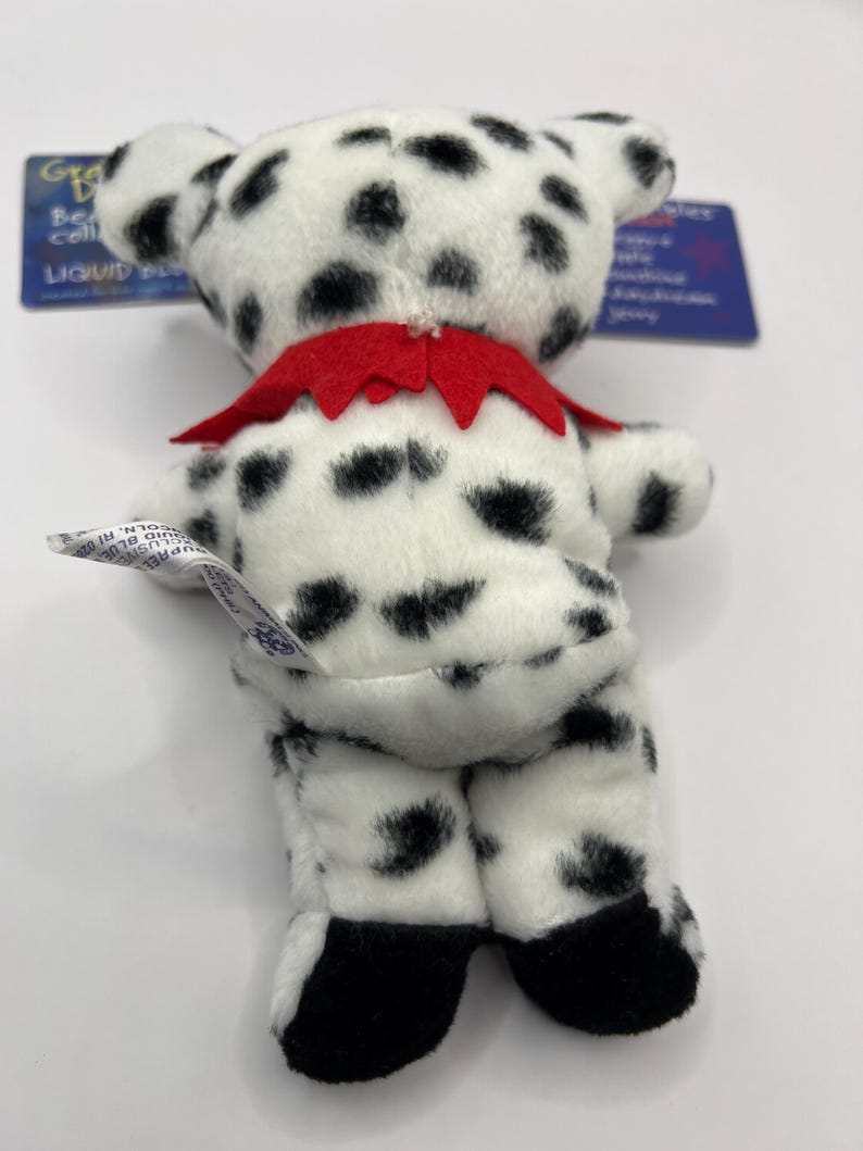 May include: A black and white dalmatian plush toy with a red collar. The toy is standing on a white surface.