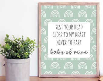 May include: A framed print with a light green background and white rainbow pattern. The print features the text "Rest your head close to my heart never to part baby of mine".