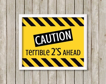 Puede incluir: Un cartel de precaución amarillo y negro con el texto "CAUTION" en un rectángulo negro y el texto "TERRIBLE 2'S AHEAD" en negro.