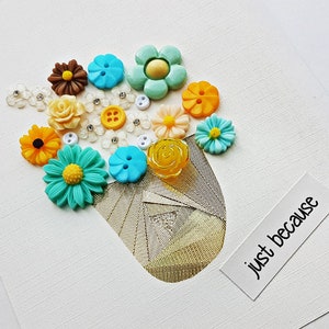 May include: A white card with a gold vase filled with colourful button flowers. The vase is made of gold mesh fabric. The card has the text "just because" written on it.