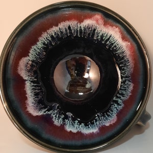May include: A black ceramic bowl with a white and red rim. The bowl has a glossy finish and a unique design with white streaks.