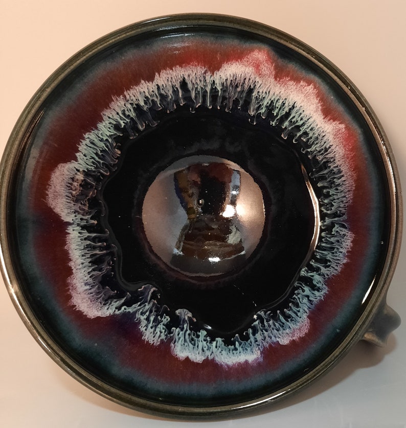 May include: A black ceramic bowl with a white and red rim. The bowl has a glossy finish and a unique design with white streaks.