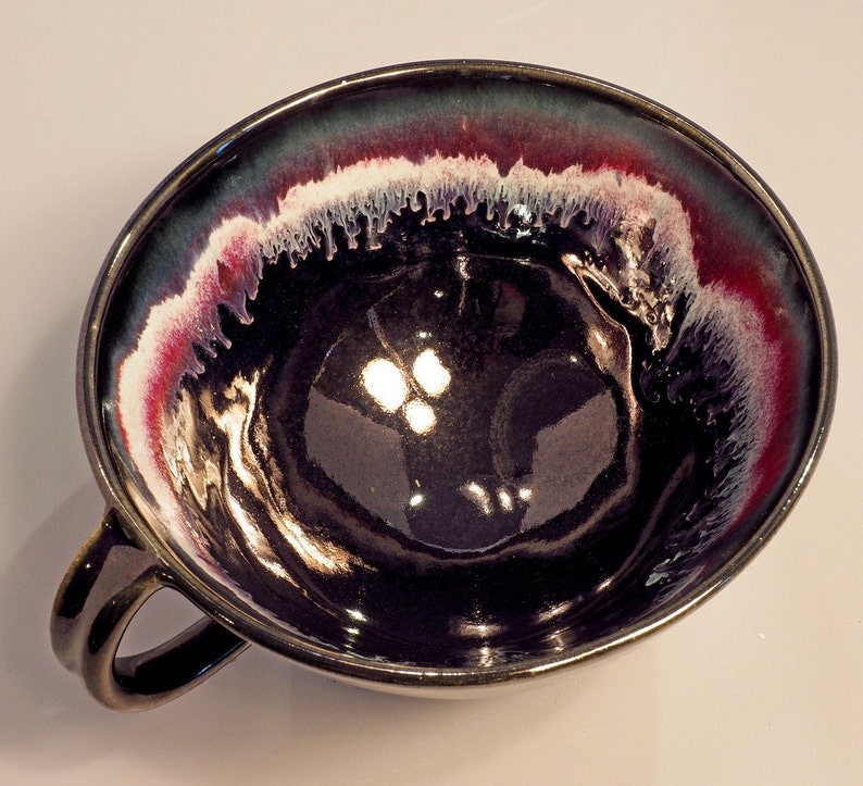 May include: A black ceramic bowl with a white and red rim. The bowl has a glossy finish and a unique, hand-painted design.