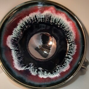 May include: A large, round ceramic bowl with a dark blue glaze and a white and red rim. The bowl has a unique, swirling design in the glaze.