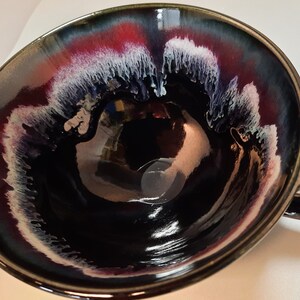 May include: A black ceramic mug with a white and red glaze design. The mug has a rounded shape and a handle.