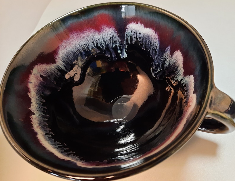 May include: A black ceramic mug with a white and red glaze design. The mug has a rounded shape and a handle.