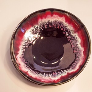 May include: A large, round ceramic bowl with a dark purple interior and a red and white rim. The rim has a white glaze with a red glaze on the outside.