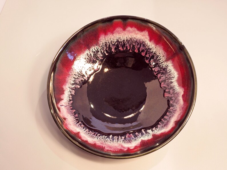 May include: A large, round ceramic bowl with a dark purple interior and a red and white rim. The rim has a white glaze with a red glaze on the outside.