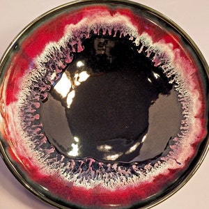 May include: A black ceramic bowl with a deep red and white rim. The rim has a unique, textured design that resembles dripping paint.