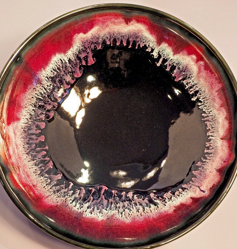 May include: A black ceramic bowl with a deep red and white rim. The rim has a unique, textured design that resembles dripping paint.