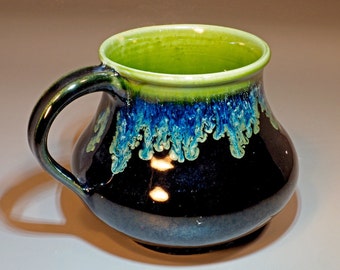 May include: A green and blue glazed ceramic mug with a rounded body and a handle. The mug has a dark blue glaze with green and blue accents.