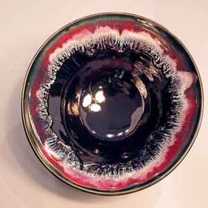 May include: A black ceramic bowl with a red and white rim. The bowl has a glossy finish and a unique, swirling design.