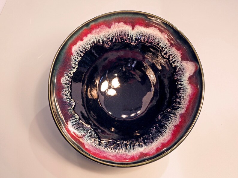 May include: A black ceramic bowl with a red and white rim. The bowl has a glossy finish and a unique, swirling design.