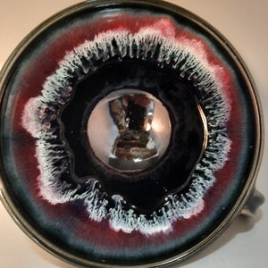 May include: A ceramic mug with a dark blue glaze and a white and red rim. The inside of the mug is glazed with a shiny, reflective finish.