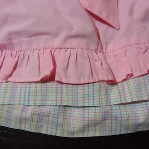 May include: A pink skirt with a ruffled hem and a plaid lining. The plaid is a mix of pink, yellow, and blue.