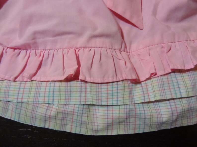 May include: A pink skirt with a ruffled hem and a plaid lining. The plaid is a mix of pink, yellow, and blue.