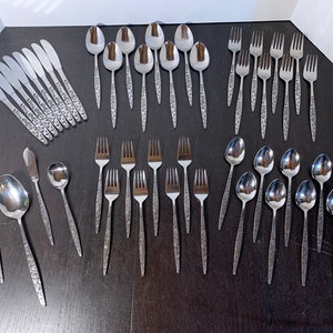 May include: A set of stainless steel silverware with an ornate design. The set includes spoons, forks, and knives.