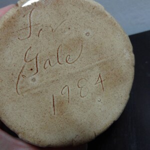 May include: Close-up of a beige ceramic object with the inscription "Fran Gale 1984" in brown ink.