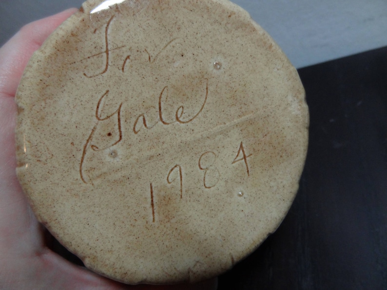 May include: Close-up of a beige ceramic object with the inscription "Fran Gale 1984" in brown ink.