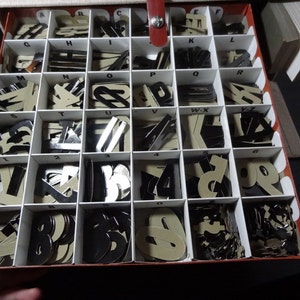 May include: A red and white box with compartments filled with black and white letter and number tiles. The box is open and the tiles are visible.