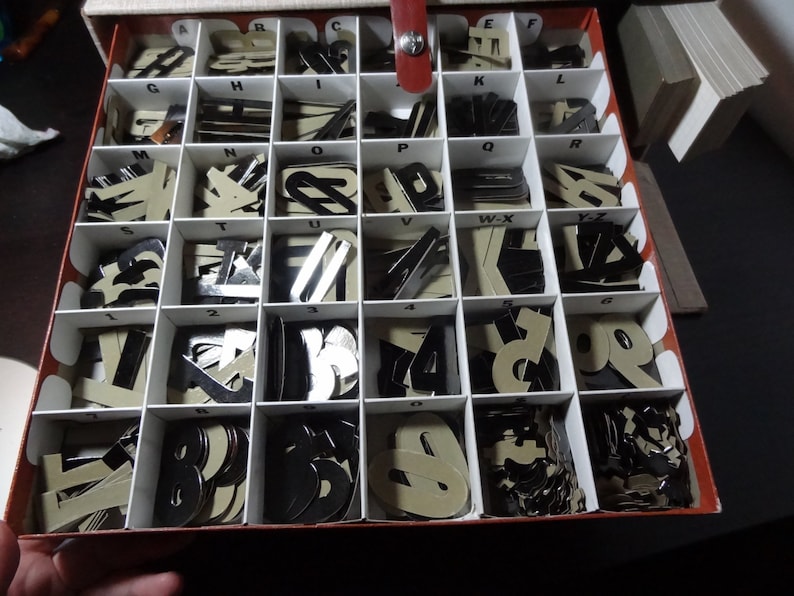 May include: A red and white box with compartments filled with black and white letter and number tiles. The box is open and the tiles are visible.