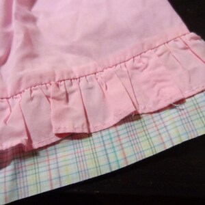 May include: A pink skirt with a ruffled hem and a plaid lining. The skirt is made of a soft, lightweight fabric.