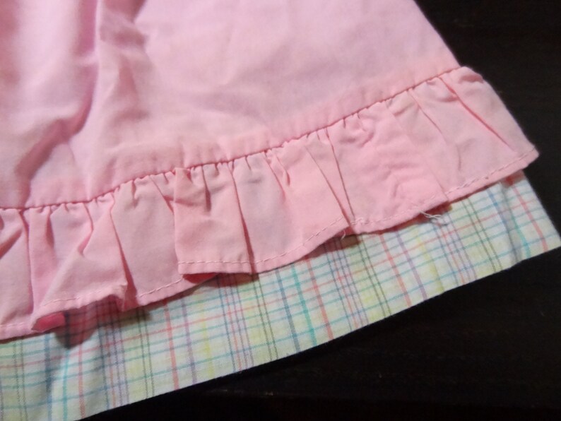 May include: A pink skirt with a ruffled hem and a plaid lining. The skirt is made of a soft, lightweight fabric.