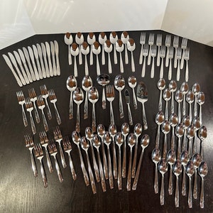 May include: A set of silverware, including forks, knives, and spoons, laid out on a dark wooden surface. The silverware is made of polished stainless steel and has a traditional design.