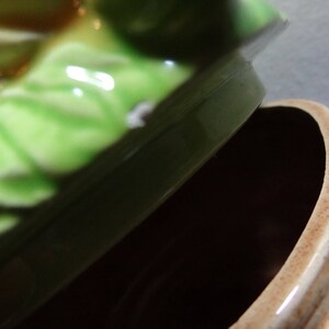 May include: A green and brown ceramic cookie jar with a lid shaped like a cabbage. The lid has a white spot on it.
