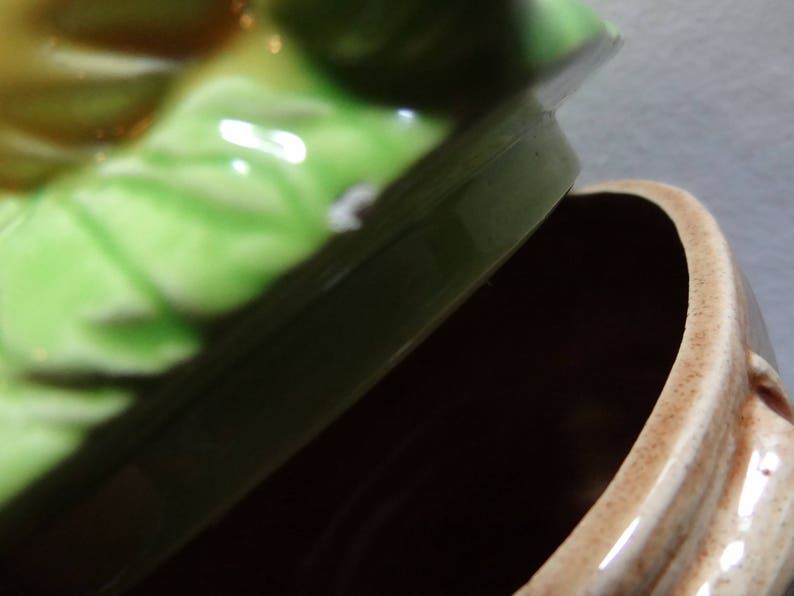 May include: A green and brown ceramic cookie jar with a lid shaped like a cabbage. The lid has a white spot on it.