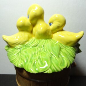May include: A ceramic birdhouse with three yellow birds perched on a green nest. The birdhouse is shaped like a barrel and has a brown base.