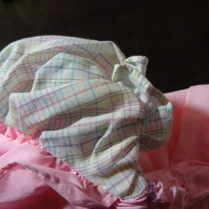 May include: A pink and white plaid fabric with a ruffled edge. The fabric is gathered and folded, creating a soft, layered look.