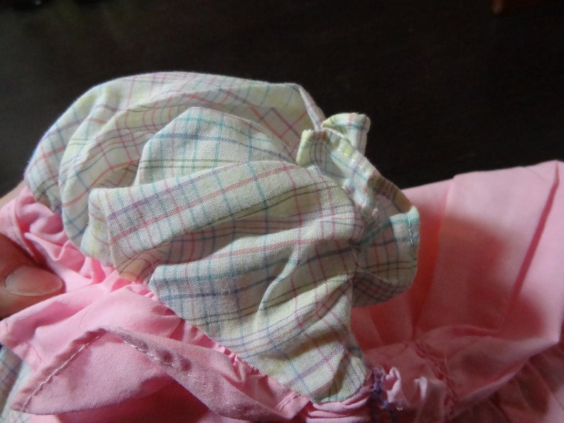 May include: A pink and white plaid fabric with a ruffled edge. The fabric is gathered and folded, creating a soft, layered look.