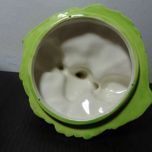 May include: Green ceramic lid with a white interior. The lid has a scalloped edge and a textured surface.