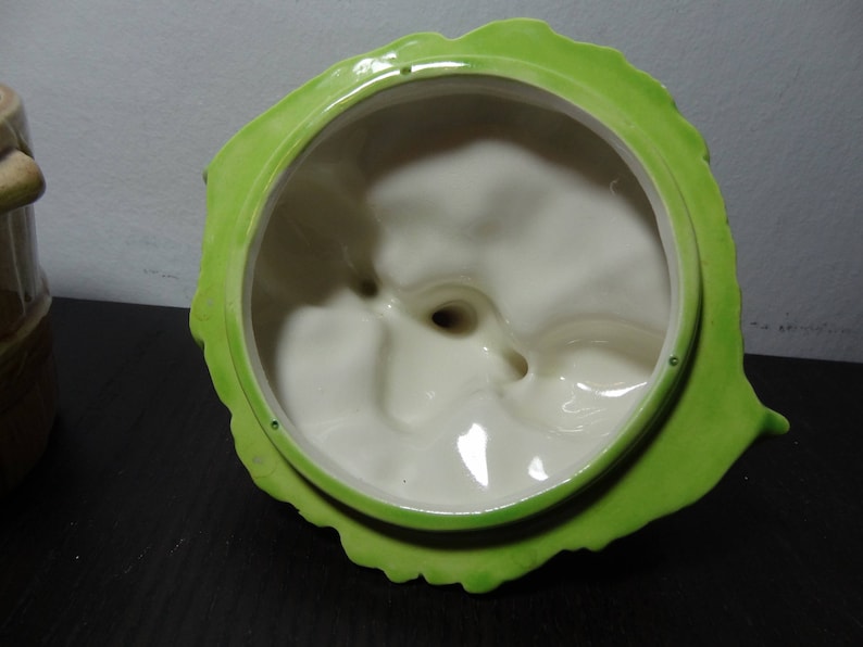 May include: Green ceramic lid with a white interior. The lid has a scalloped edge and a textured surface.