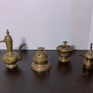 May include: Four ornate brass decorative items, including two small teapots, a round incense burner, and a lidded bowl. The items are all intricately decorated with floral and geometric patterns.