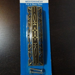 May include: A gold-toned metal door pull and back plate with an ornate design. The packaging says "Mediterranean Pull & Back Plate 4 1/2" center".