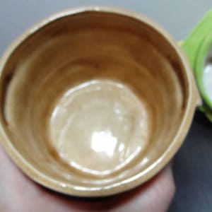 May include: A close-up of the inside of a ceramic jar with a brown glaze. The jar is empty and has a smooth, rounded interior.