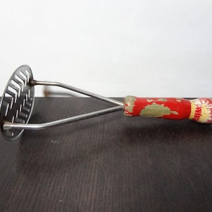 May include: A vintage red and white wooden handled potato masher with a stainless steel mashing surface.