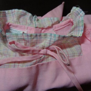 May include: A pink dress with a plaid collar and a bow tie. The dress has a ruffled collar and a tie that can be tied in the front.