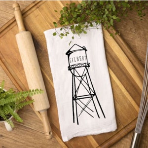 May include: White kitchen towel with a black and white illustration of a water tower with the word "GILBERT" printed on it.