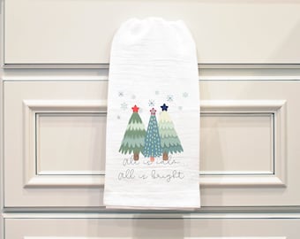 May include: White kitchen towel with a Christmas tree design. The trees are green, blue, and white with red and blue stars on top. The text on the towel reads "all is calm... all is bright..."