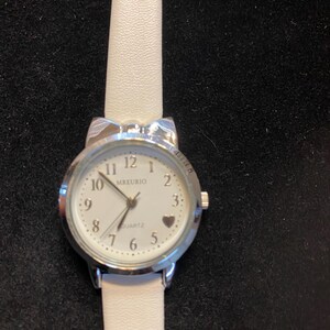 May include: A silver-toned quartz watch with a white face and a white leather band. The watch face features black numerals, a heart-shaped marker, and the brand name "MREURIO". The band is approximately 0.5 inches wide.