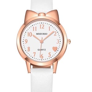 May include: A white wristwatch with a rose gold case and a white leather band. The watch face is white with black numerals and a heart at the 5 o'clock position. The watch has a bow-shaped top and the brand name "MREURIO".
