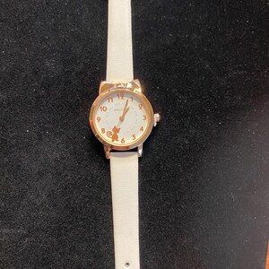 May include: A white wristwatch with a gold-colored cat ear-shaped bezel. The watch face is white with gold-colored numerals and hands. The watch has a white leather strap.