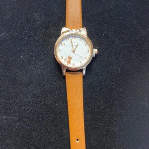 May include: A gold-toned wristwatch with a white face and brown leather band. The watch face features black numerals and a small cartoon character. The band is a light brown color and has a buckle closure.