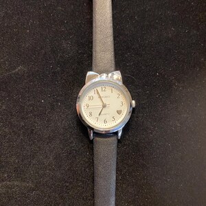 May include: A silver-toned wristwatch with a white face and black leather band. The watch face has black numerals and a small heart at the 3 o'clock position. The band is approximately 0.5 inches wide.