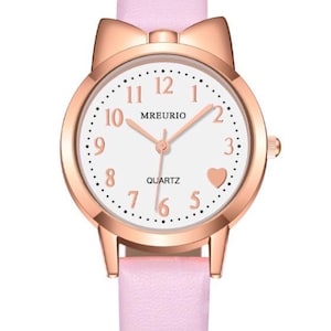 May include: A pink quartz watch with a rose gold case and a matching pink leather strap. The watch face is white with black numerals and a heart-shaped detail. The watch has a bow-shaped detail at the top.
