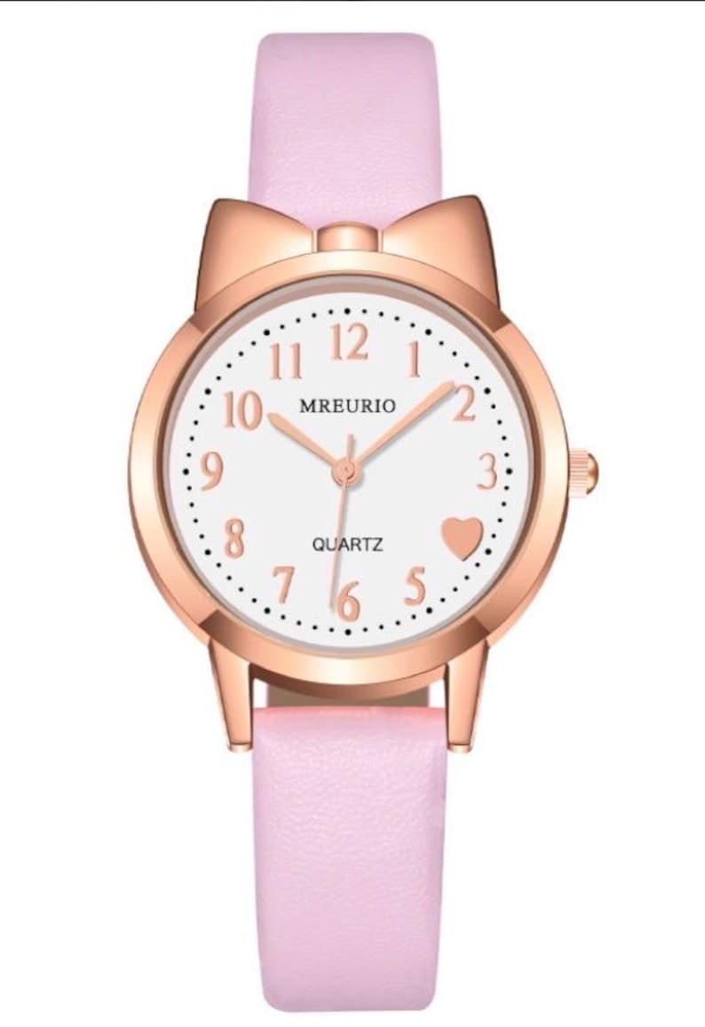 May include: A pink quartz watch with a rose gold case and a matching pink leather strap. The watch face is white with black numerals and a heart-shaped detail. The watch has a bow-shaped detail at the top.